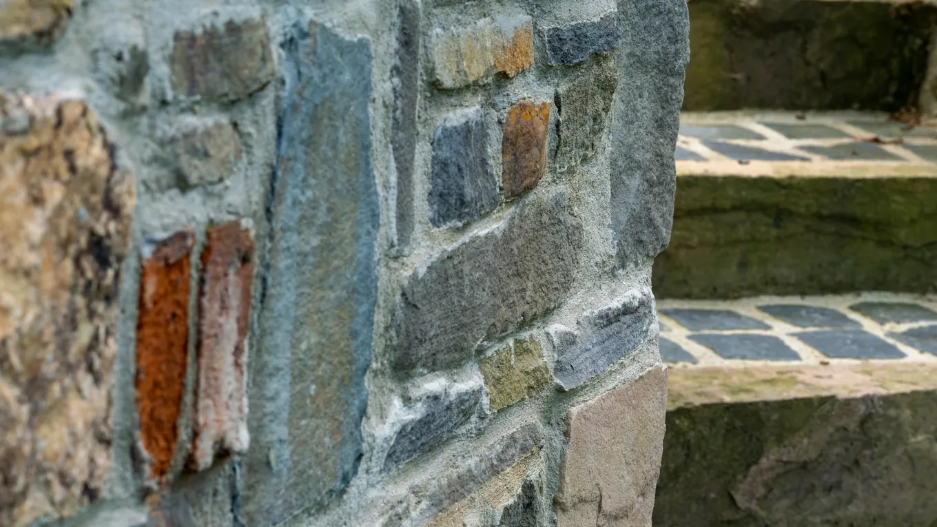 Ecke einer Bruchsteinmauer neben Stufen aus Naturstein mit Kleinpflaster