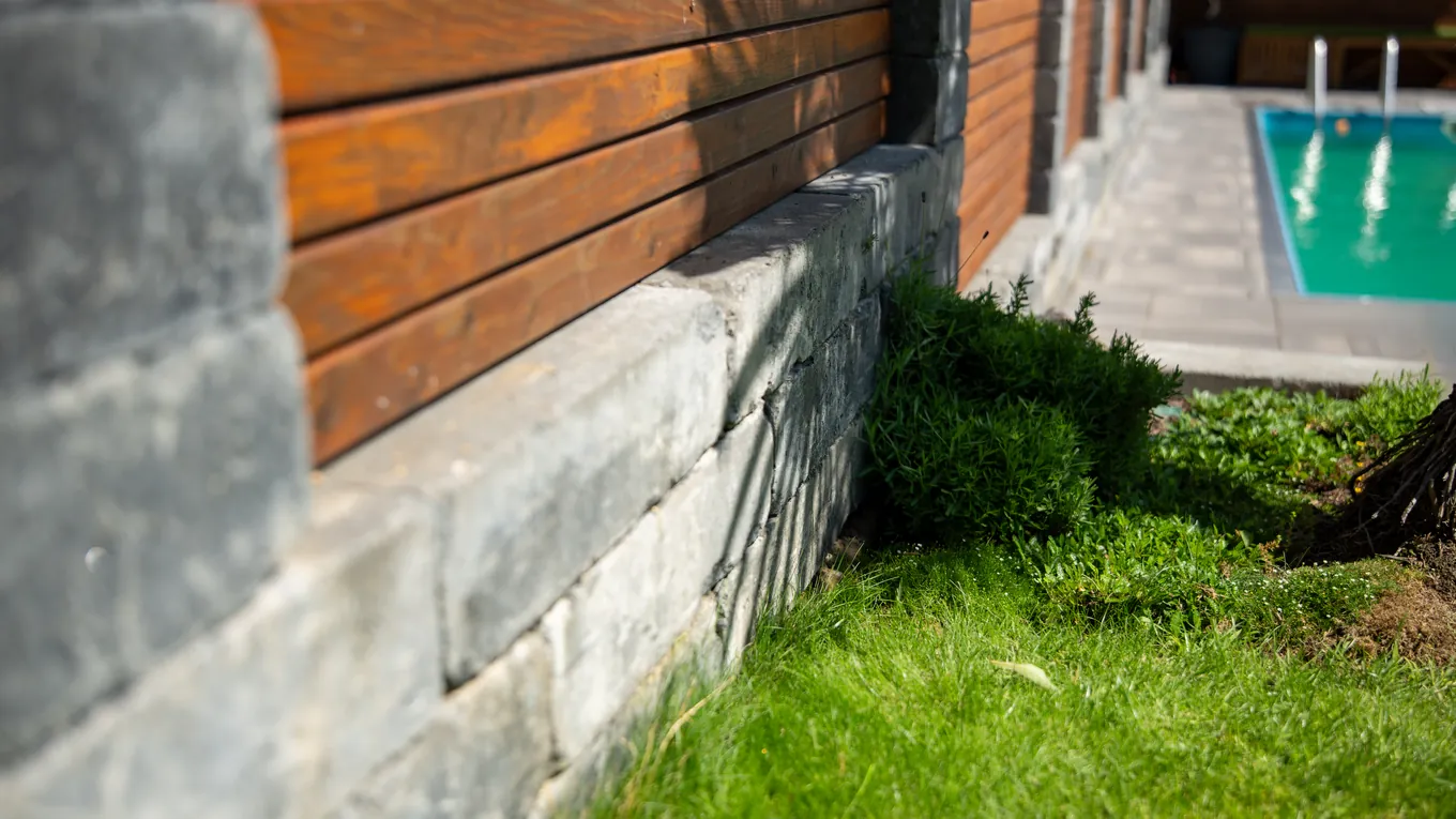 Blick über eine Natursteinmauer mit Holzsichtschutz auf einen Pool mit Edelstahlleiter